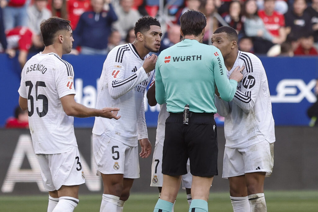 El delantero francés del Real Madrid Kylian Mbappé y su compañero el delantero inglés Jude Bellingham conversan con el el colegiado Munuera Montero, durante el partido de la jornada 24 de la LaLiga EA Sports, disputado este sábado en el estadio el Sadar de Pamplona. EFE/ Villar Lopez