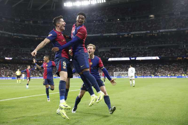 El delantero polaco del FC Barcelona Robert Lewandowski (i) celebra tras anotar un gol con su compañero Alejandro Balde, durante el partido de la jornada 11 de LaLiga EA Sports entre el Real Madrid y el FC Barcelona, en el estadio Santiago Bernabéu, en Madrid. EFE/Juanjo Martín