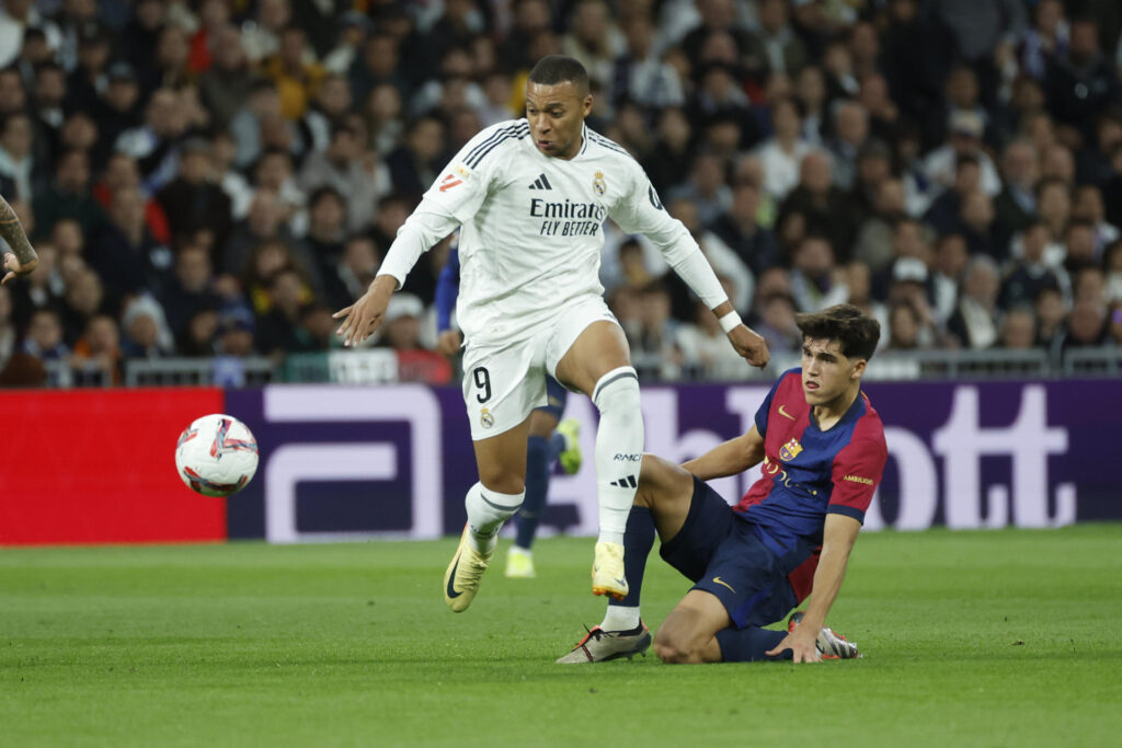 El delantero del Real Madrid Kylian Mbappé (i) lucha con Pau Cubarsí, del FC Barcelona, durante el partido de la jornada 11 de LaLiga EA Sports entre el Real Madrid y el FC Barcelona, este sábado en el estadio Santiago Bernabéu, en Madrid. EFE/Juanjo Martín