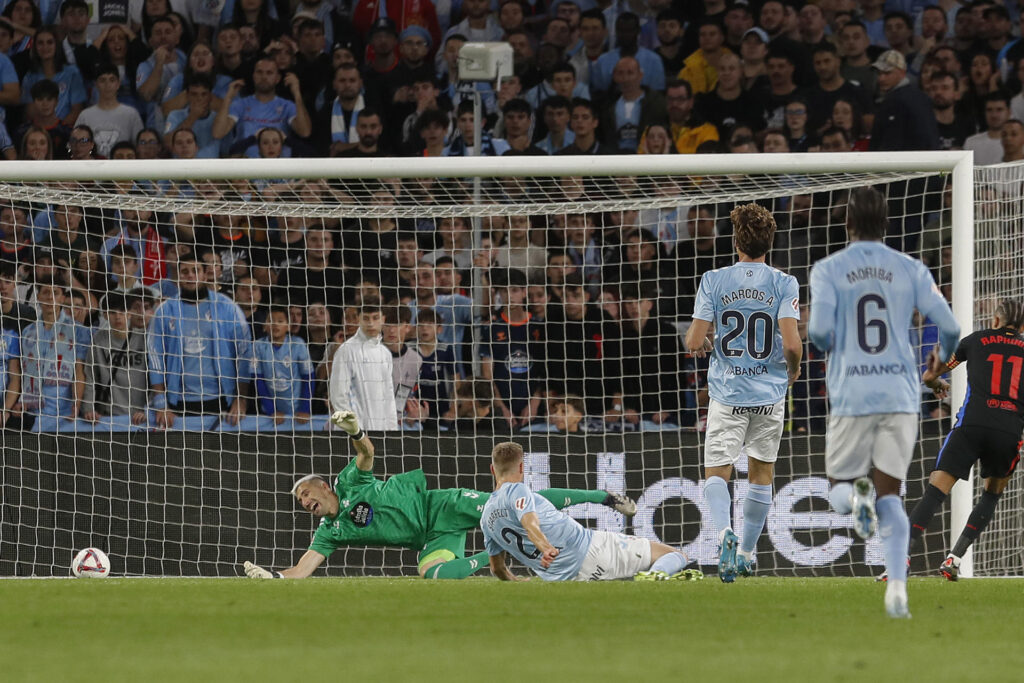 El guardameta del Celta, Vicente Guaita (i), intenta detener el remate del delantero brasileño del FC Barcelona, Raphinha (d), en la jugada que ha significado el primer gol del equipo barcelonista durante el encuentro correspondiente a la jornada 14 de Laliga EA Sports que disputan Celta y FC Barcelona en el estadio Balaidos de Vigo. EFE / Salvador Sas.